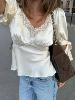 Chemisier en satin à col V bouffant et manches courtes bouffantes orné de dentelle avec ceinture à nouer dans le dos et coupe ajustée. Élégante chemise pour femme.