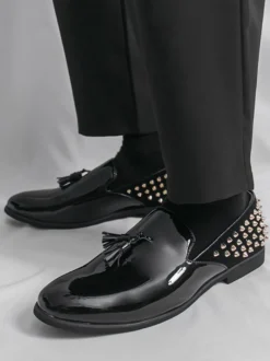 Mocassins noirs à bout rond pour homme ornés de rivets et de pompons.